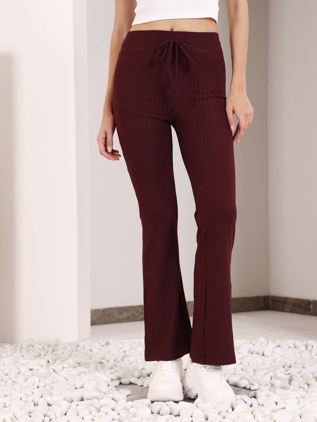 A person standing in a maroon flare pants with a drawstring waist, paired with white sneakers.