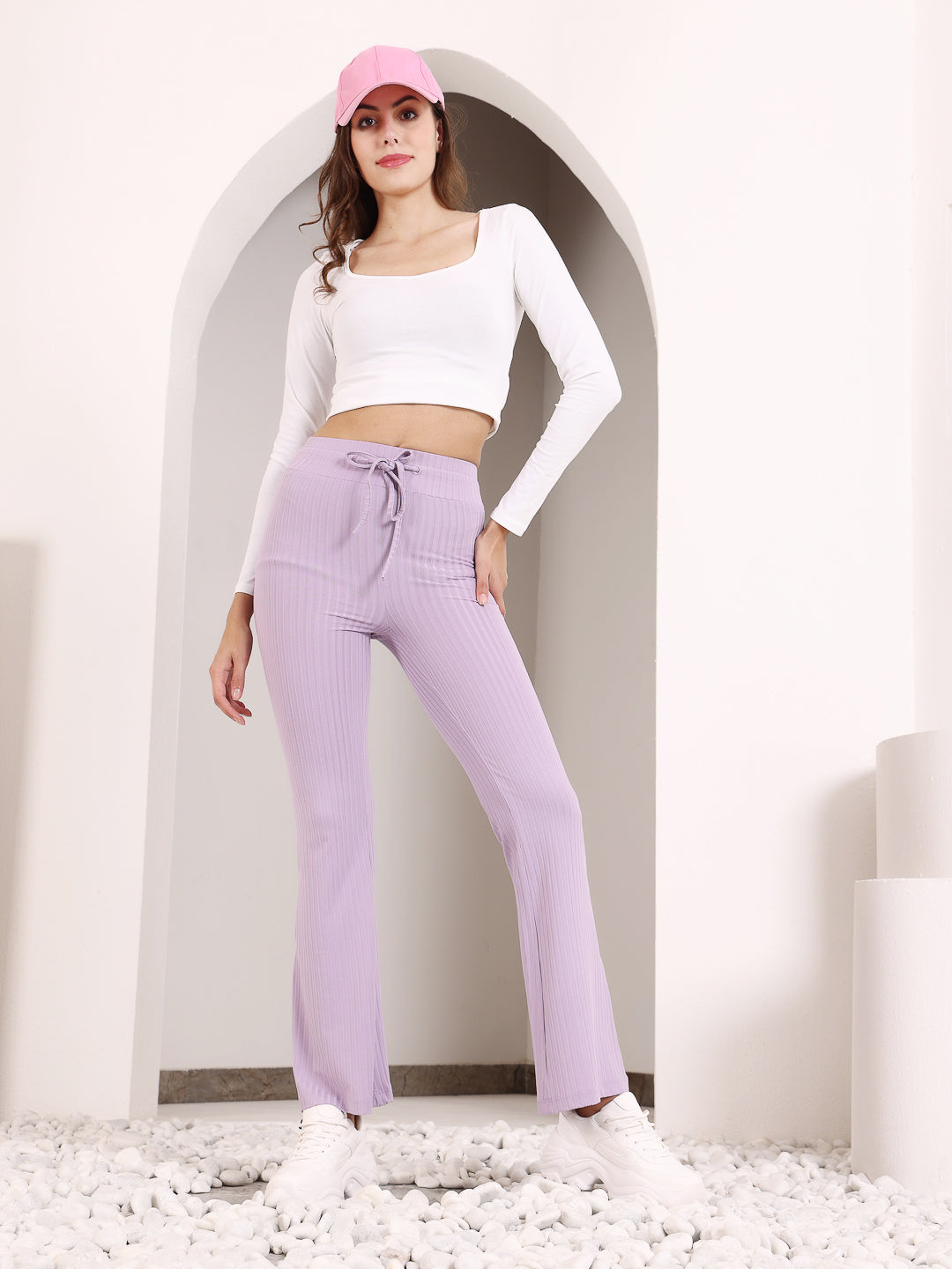 A woman standing in a doorway wearing lavender rib drawstring flare pants and a white cropped top with a bow detail.