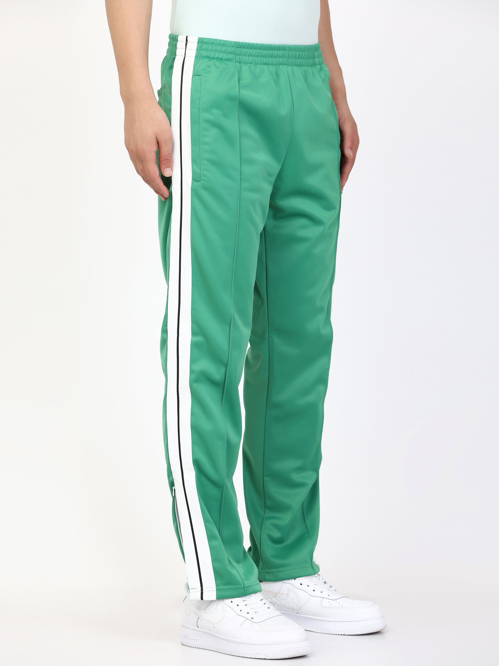 A person standing wearing green track pants with white side stripes and an elasticated waistband, with white sneakers.