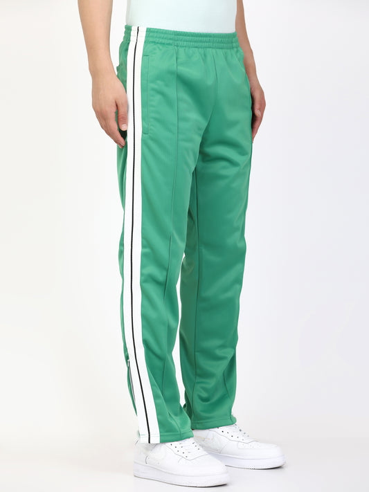 A person standing wearing green track pants with white side stripes and an elasticated waistband, with white sneakers.