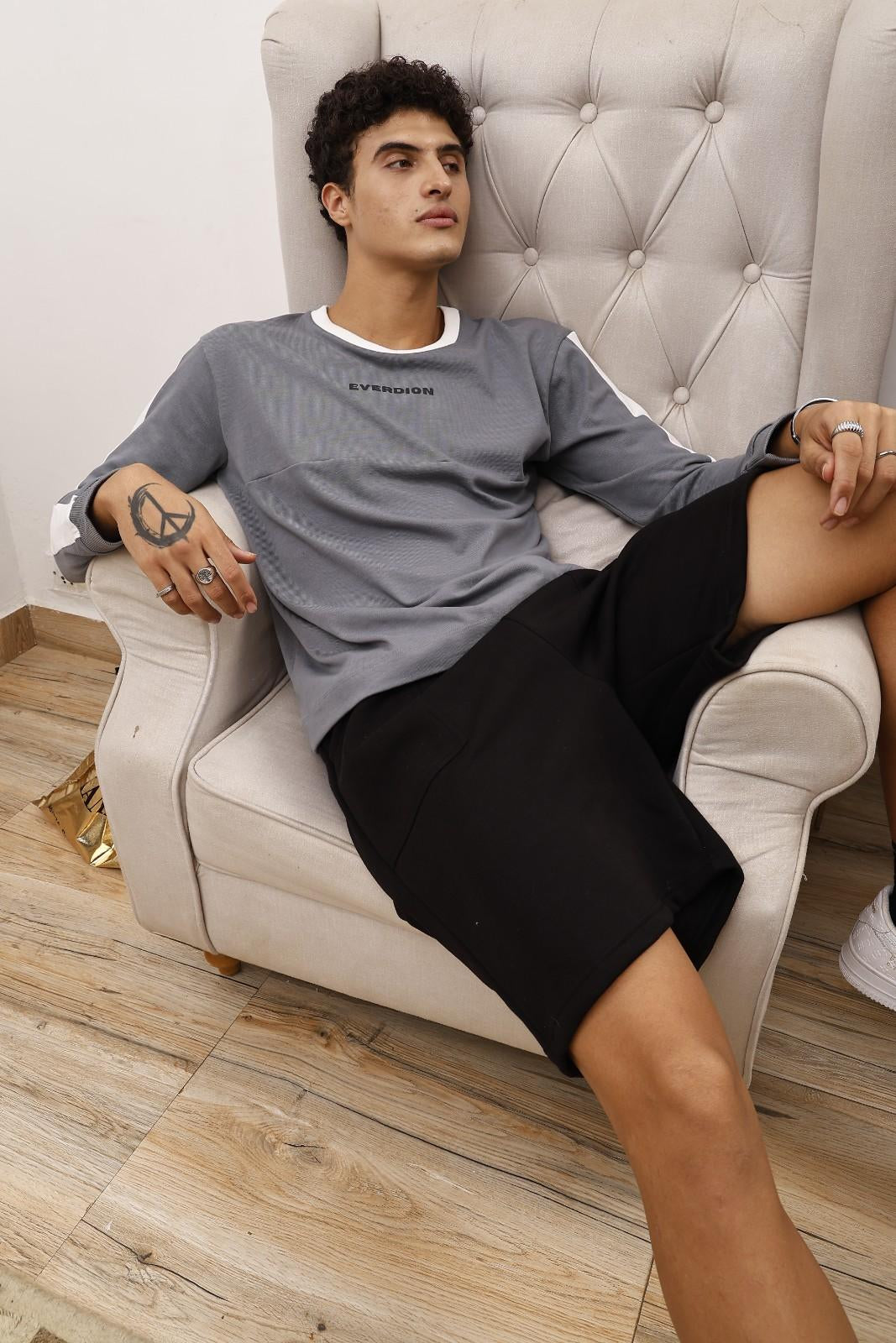 Man sitting on a white armchair wearing a gray sweatshirt and black shorts.