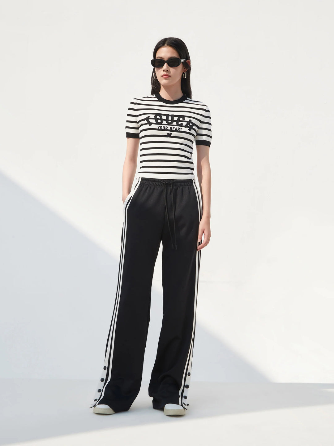 black slit snap button tracks pants with an elastic drawstring waist, featuring white stripes on the legs and a side slit on one leg