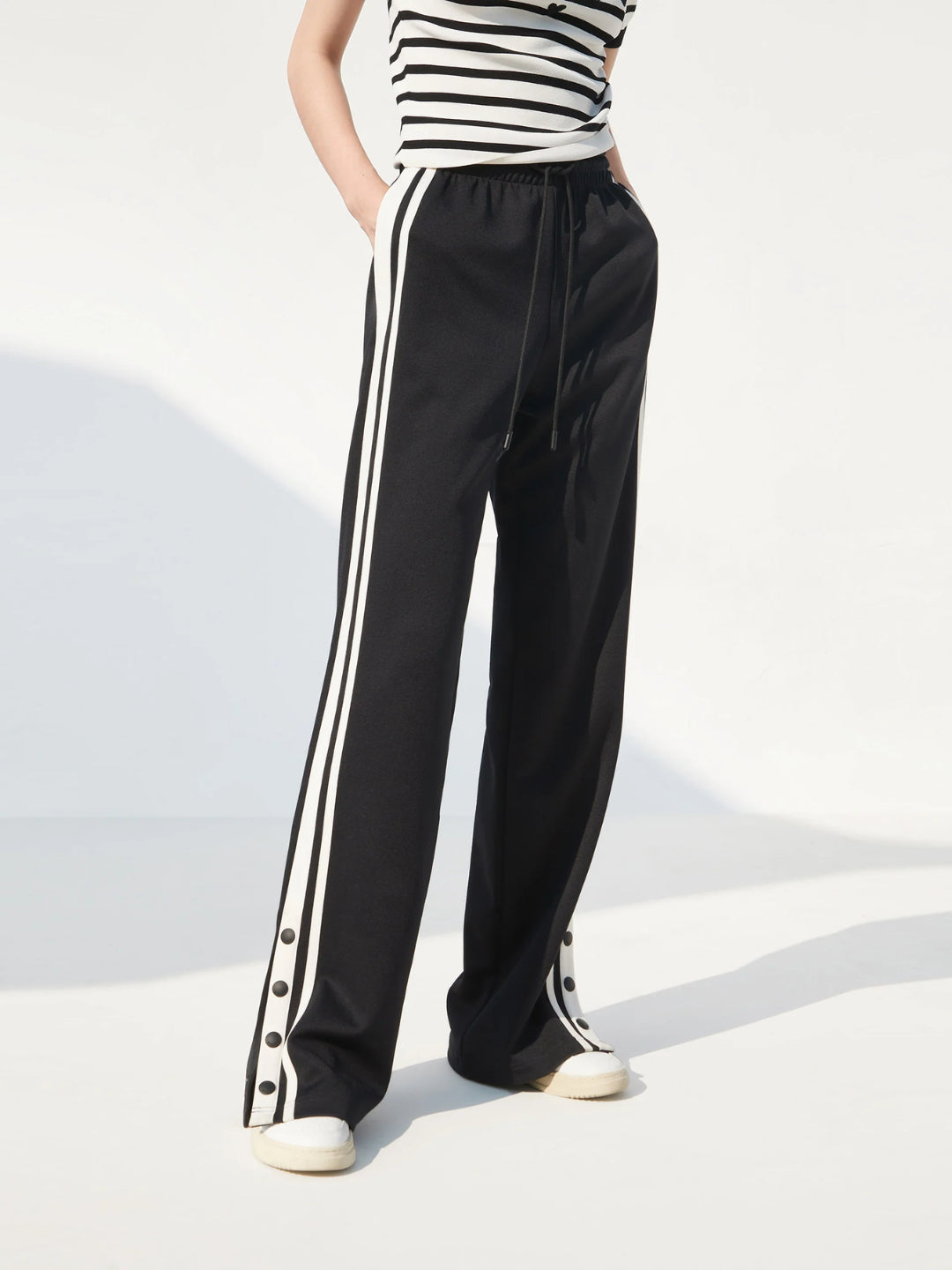 black slit snap button tracks pants with an elastic drawstring waist, featuring white stripes on the legs and a side slit on one leg