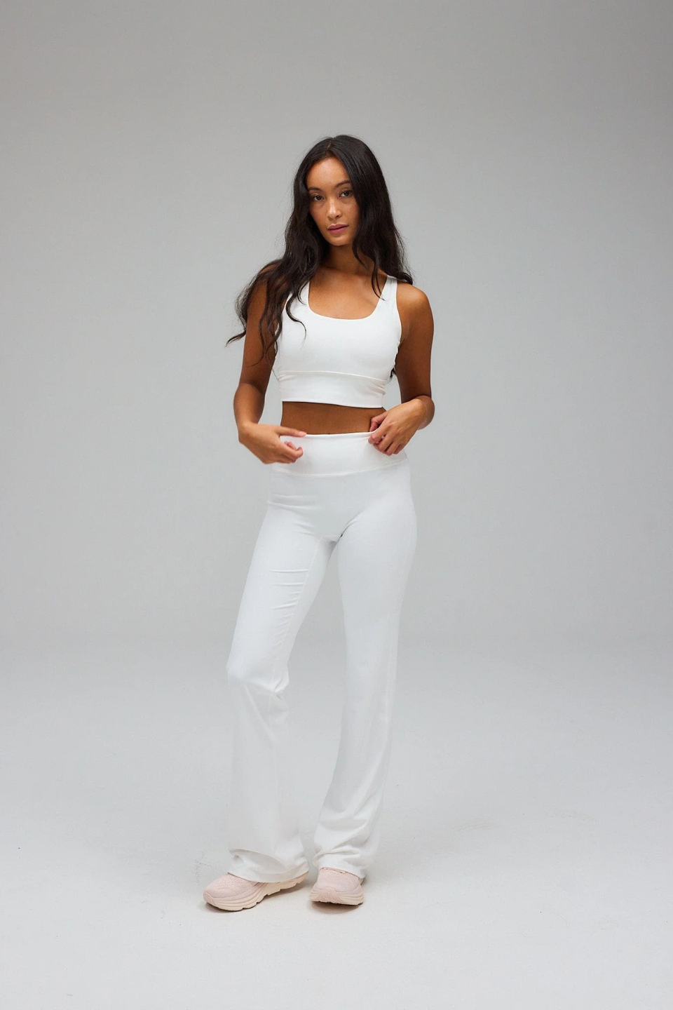 Woman wearing a white sports bra and pants on a gray background