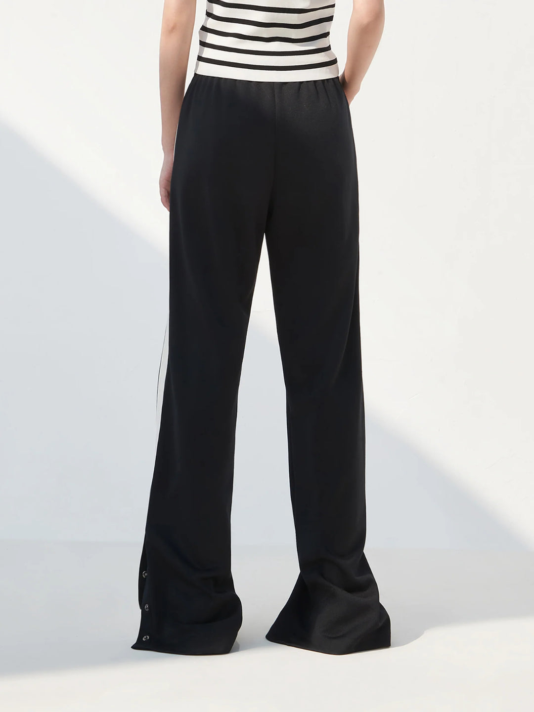 black slit snap button tracks pants with an elastic drawstring waist, featuring white stripes on the legs and a side slit on one leg