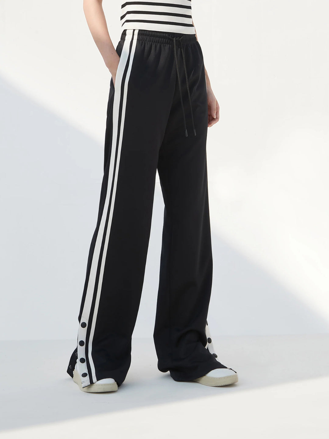 black slit snap button tracks pants with an elastic drawstring waist, featuring white stripes on the legs and a side slit on one leg