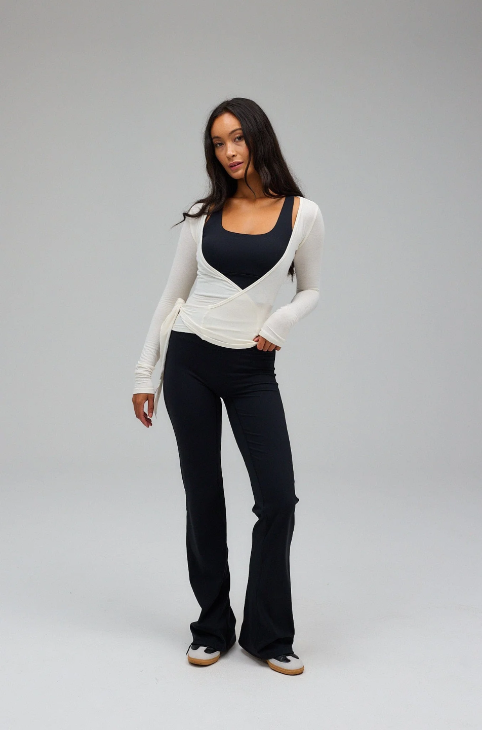 Woman wearing a white long-sleeve top and black pants on a gray background