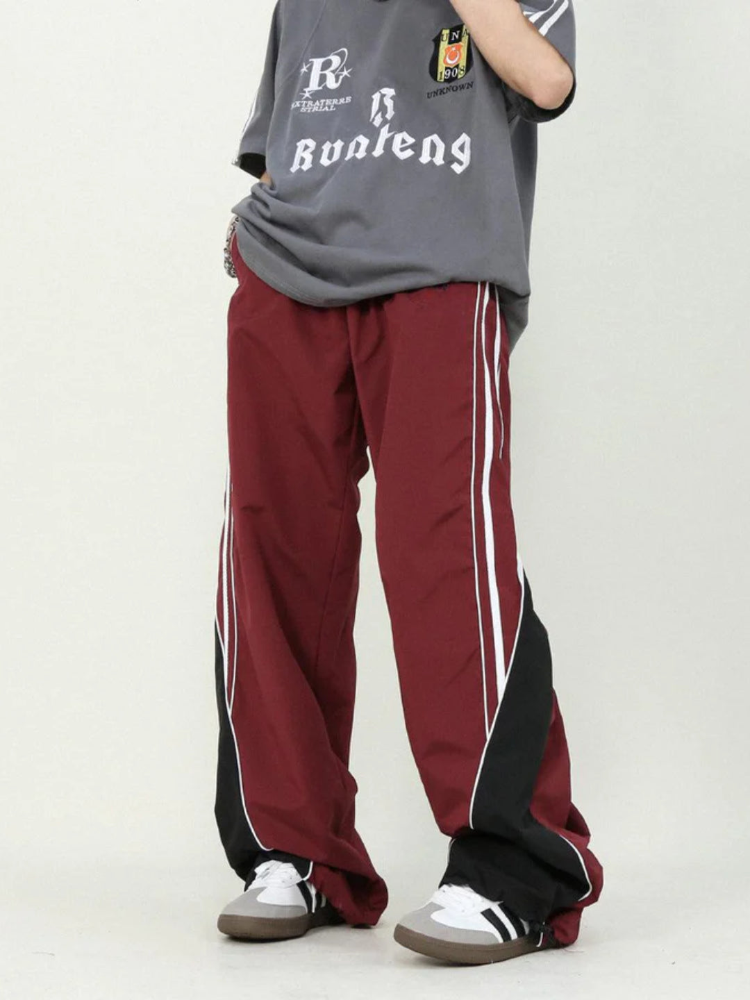 A person wearing red striped parachute pants with contrast piping, an elasticated waistband, and adjustable drawstrings.