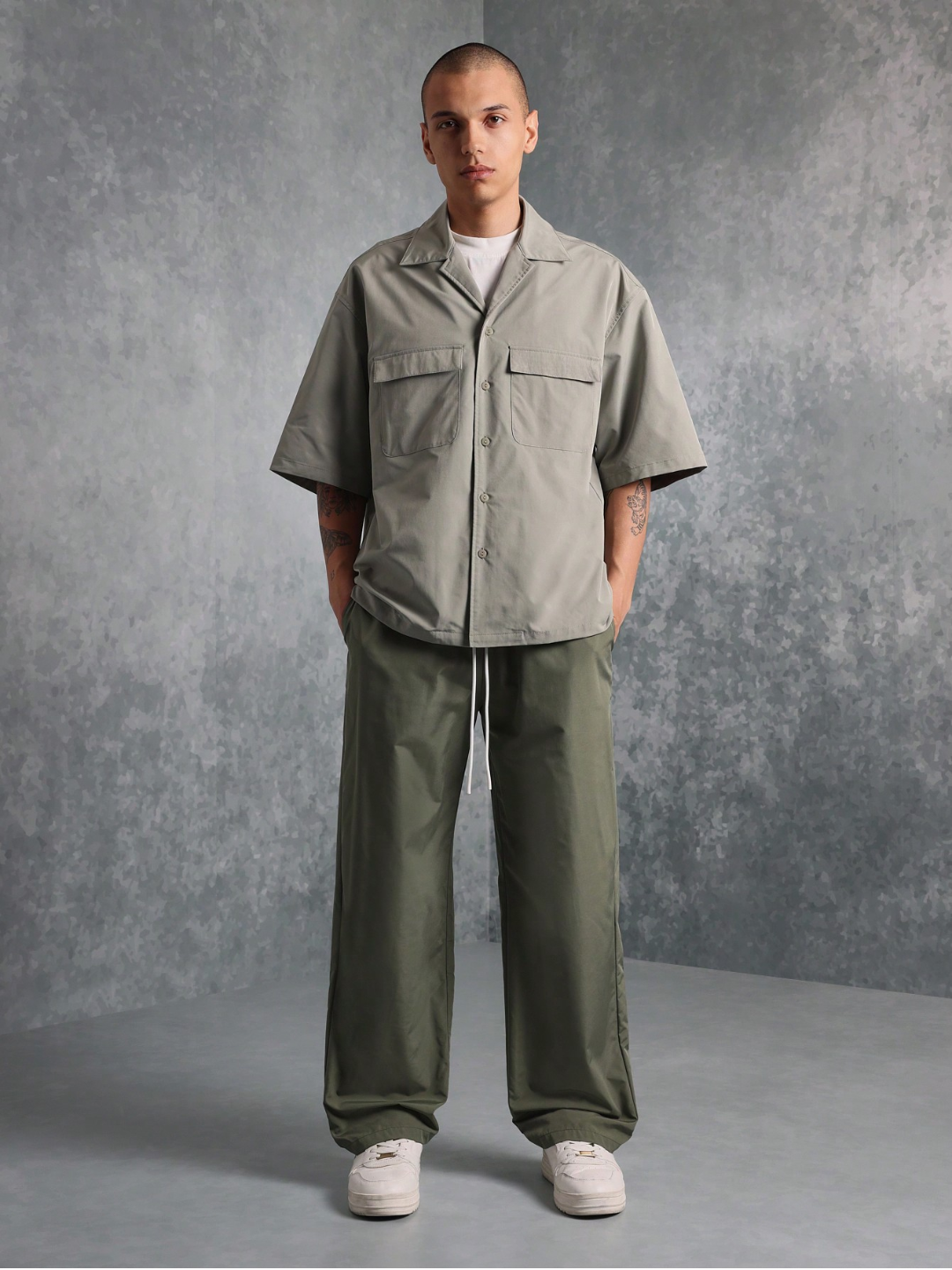 This image features the Chateau Boxy Fit Shirt and Pant set, presenting a stylish and relaxed outfit. The shirt is short-sleeved with a boxy fit and features two chest pockets, in a light grey color that complements the darker green pants.
