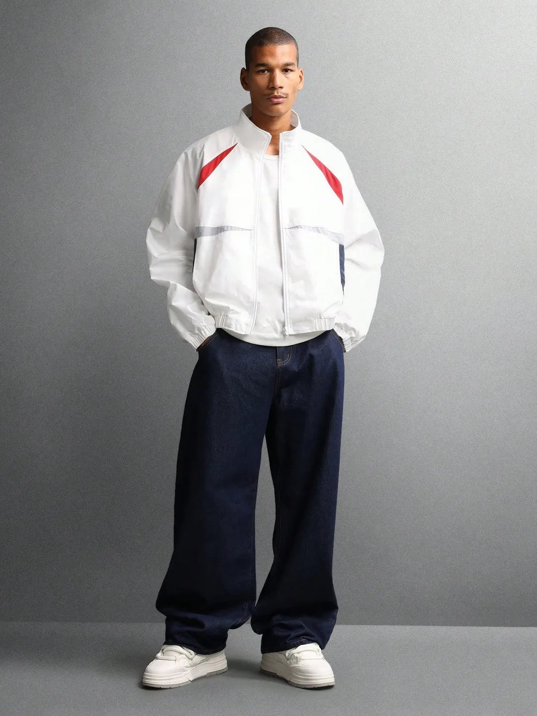 Man wearing a white jacket with red accents and dark pants on a gray background