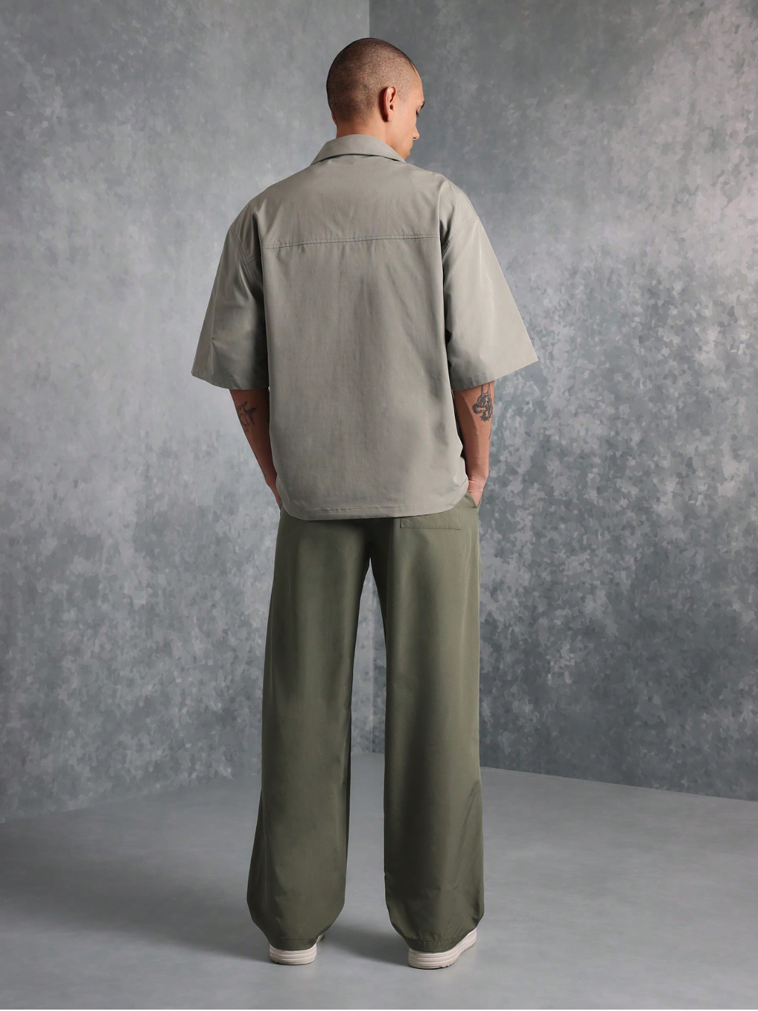 This image features the Chateau Boxy Fit Shirt and Pant set, presenting a stylish and relaxed outfit. The shirt is short-sleeved with a boxy fit and features two chest pockets, in a light grey color that complements the darker green pants.