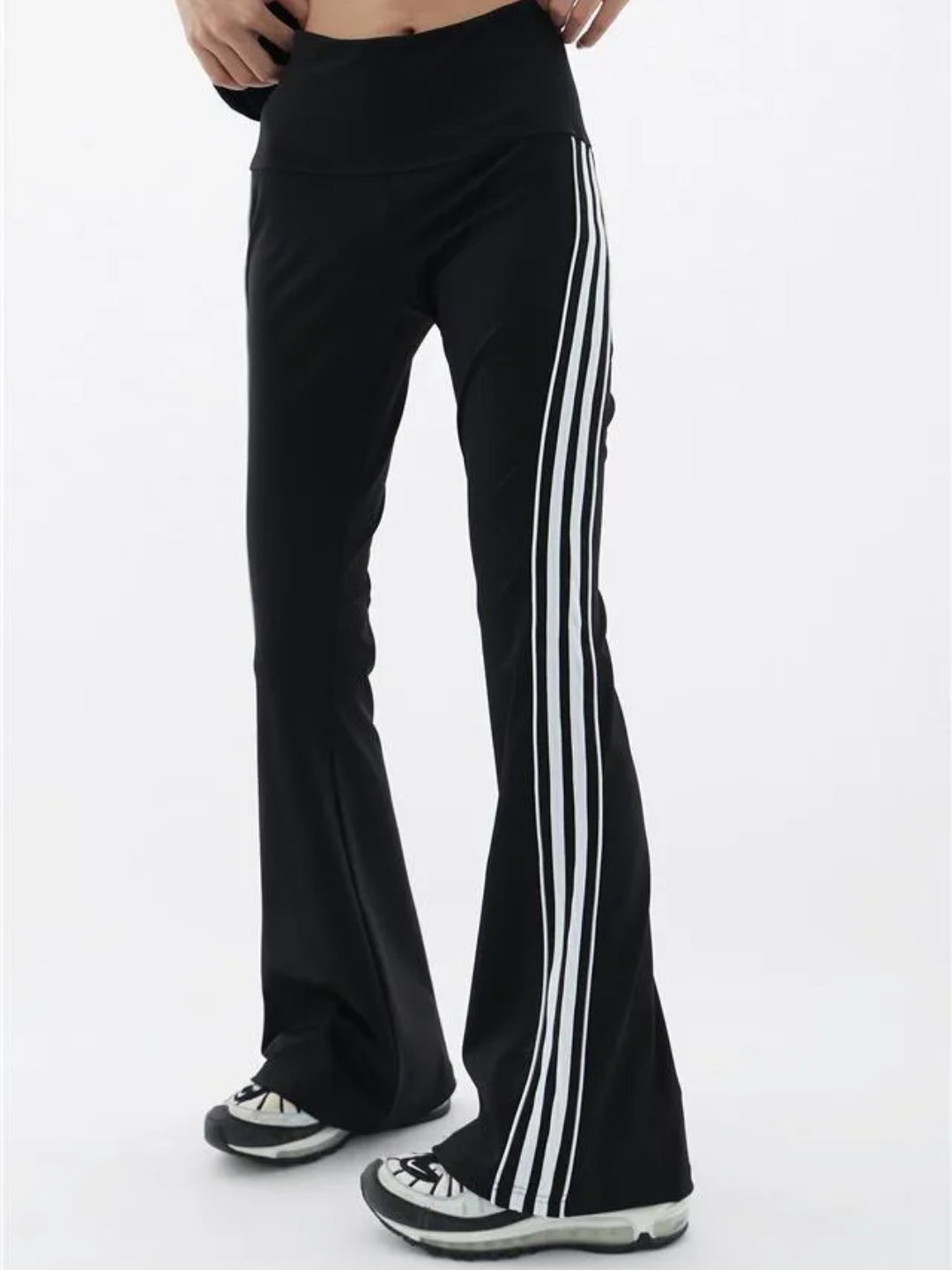 A pair of black flare leggings with white stripes on the side, modeled by a woman standing sideways.