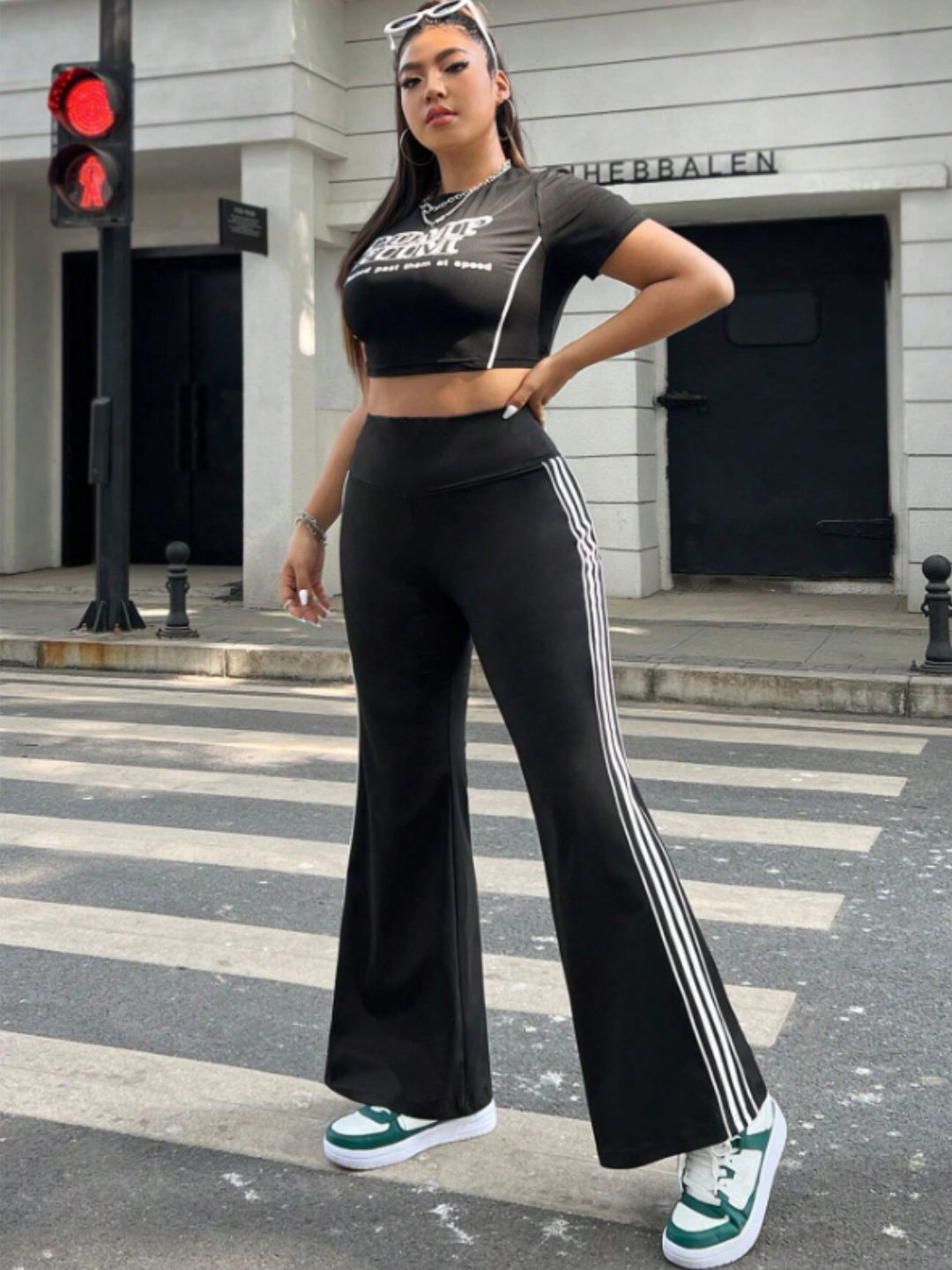 A model wearing black flare leggings with white stripes and a sports tee, standing on a crosswalk with a red traffic light in the background.