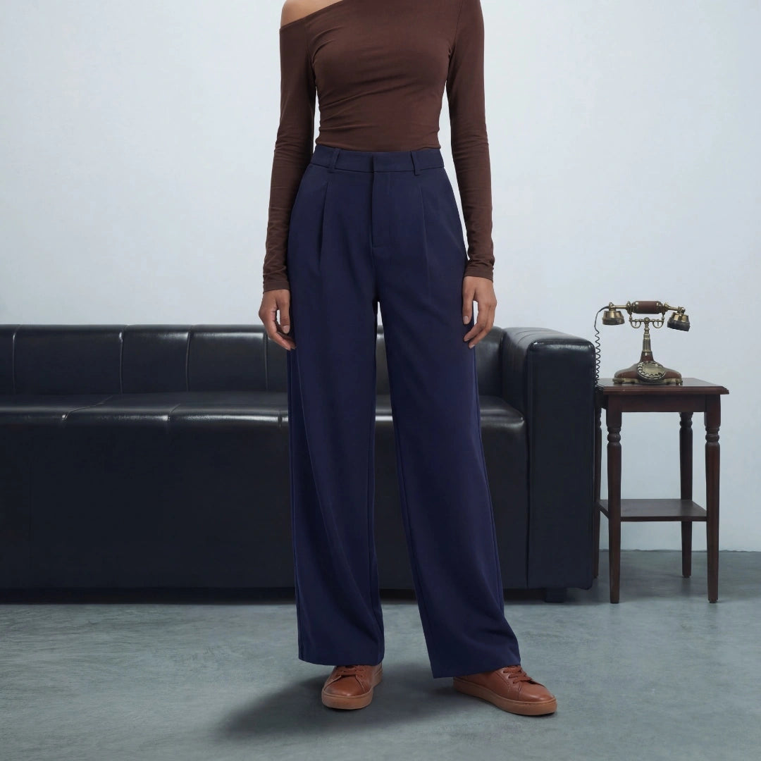 Person wearing a brown top and navy pants standing in a room with a black leather couch and wooden table.