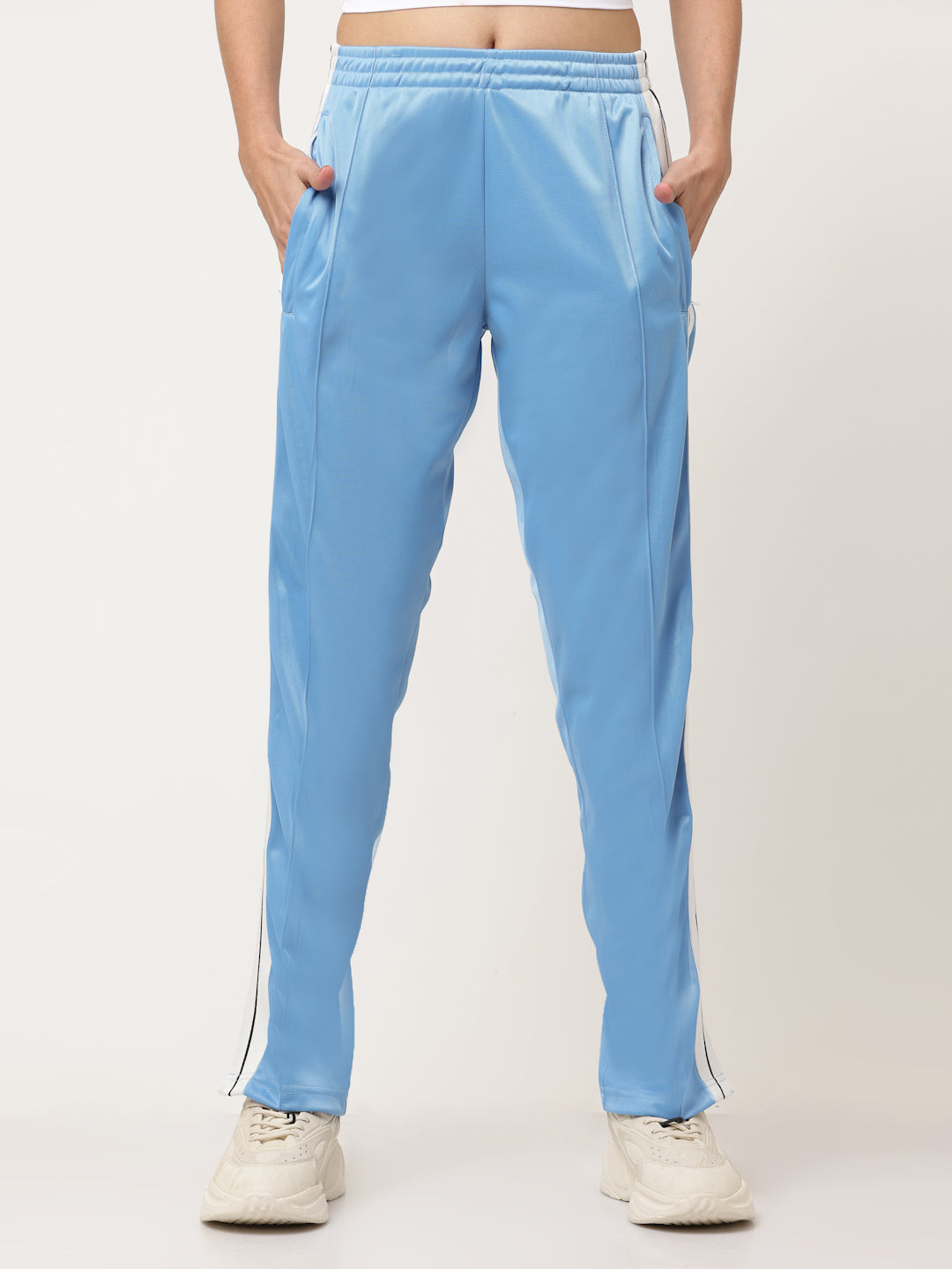 A pair of blue straight fit track pants with white side stripe detailing and a visible zipper at the bottom, held by a model.