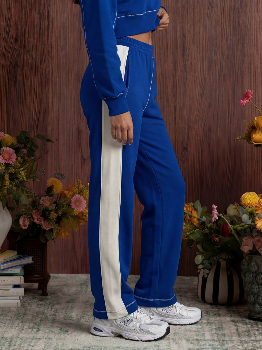 Person wearing a blue tracksuit with white stripes in a room with flowers and books.