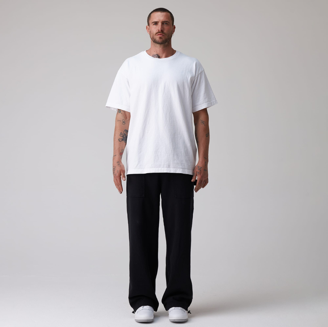 Man wearing a white t-shirt and black pants on a plain background