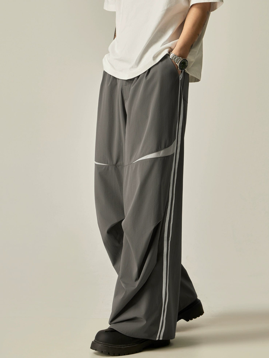 A pair of gray parachute pants with white stripes on the side, worn by a model with a white t-shirt.