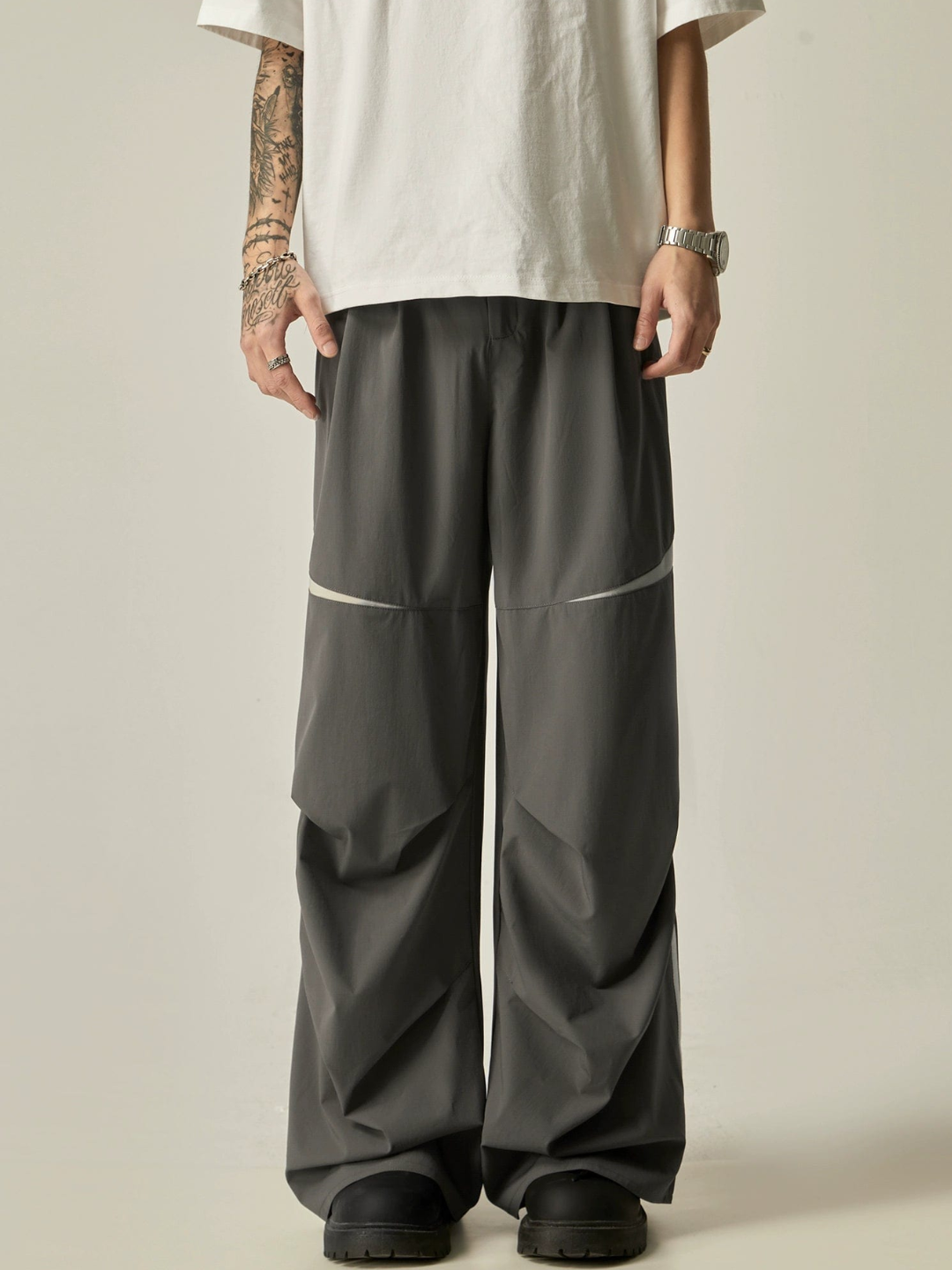 A person standing sideways, wearing a white t-shirt and navy parachute pants with white side stripes, paired with white sneakers.