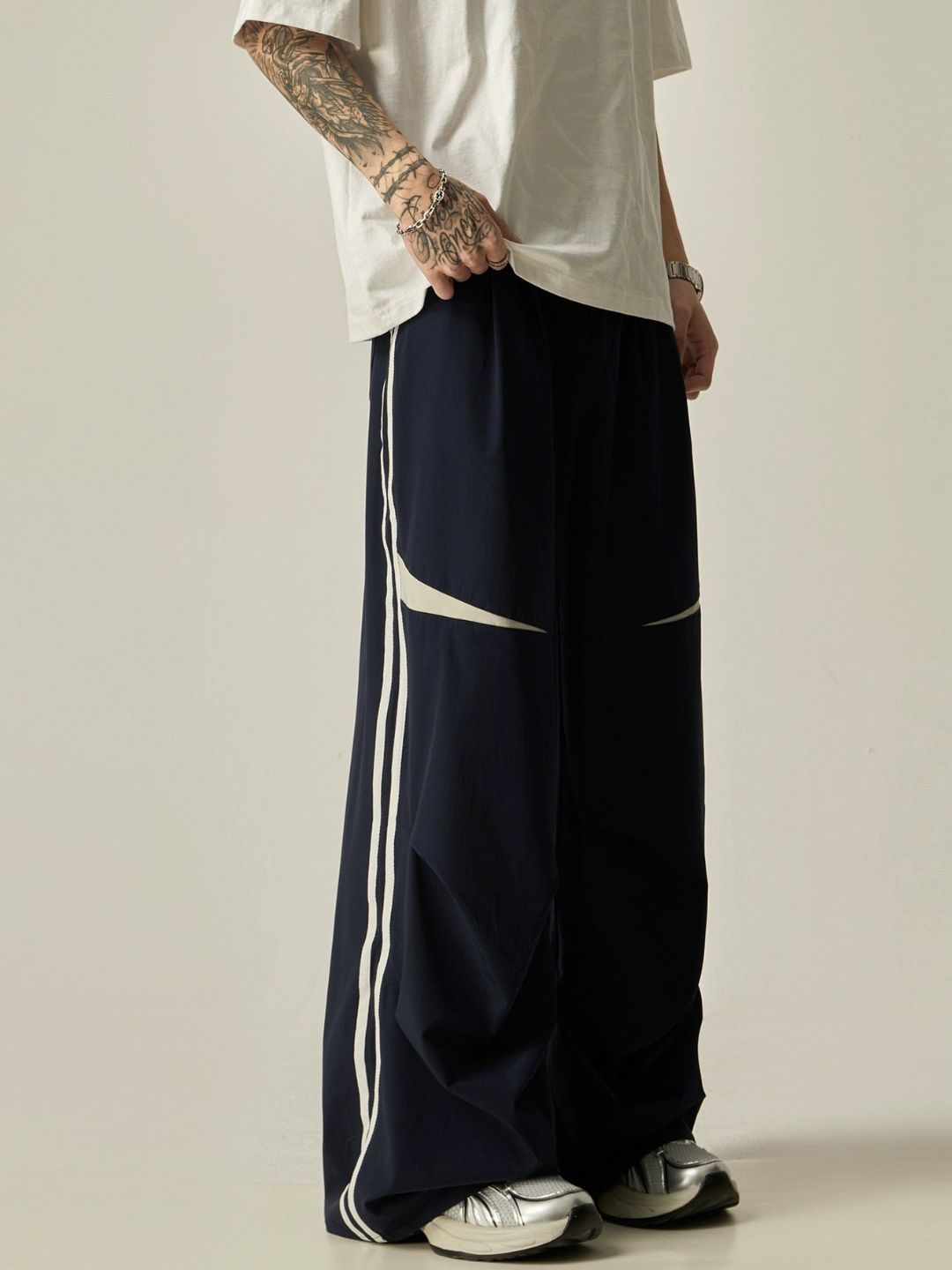 A person standing sideways, wearing a white t-shirt and navy parachute pants with white side stripes, paired with white sneakers.