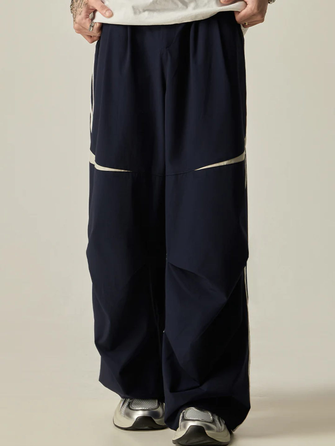 A person standing sideways, wearing a white t-shirt and navy parachute pants with white side stripes, paired with white sneakers.