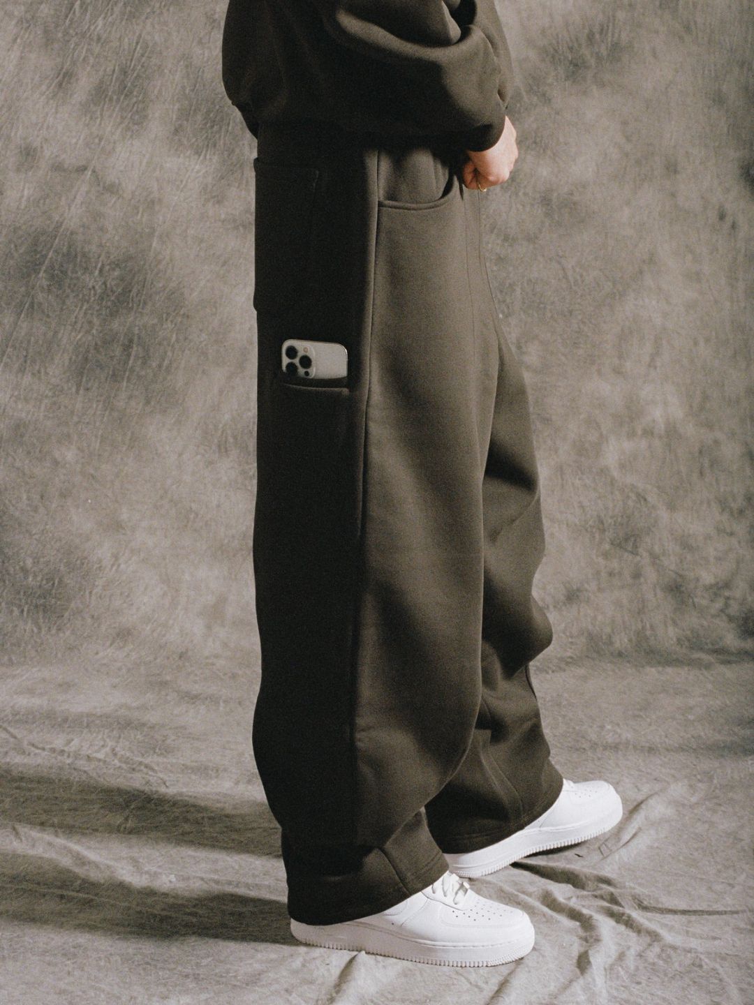 Person wearing dark green sweatpants with a pocket detail on a gray background