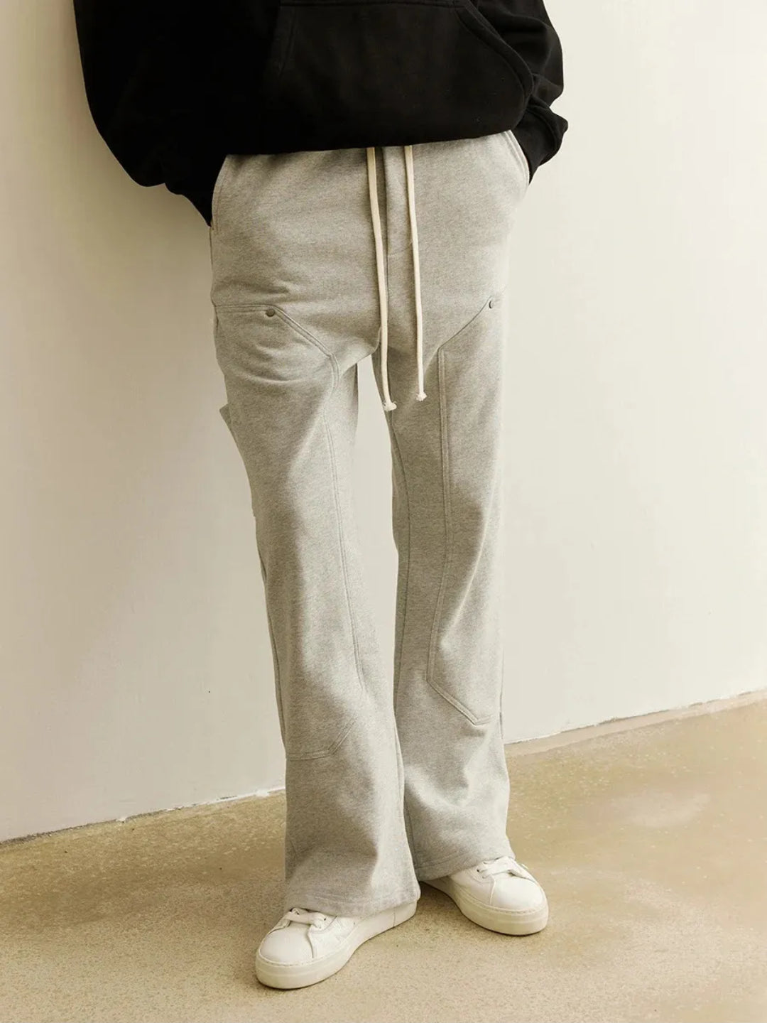 A person wearing gray sweatpants with an elastic waistband and drawcord, featuring patchwork pockets on the thigh.