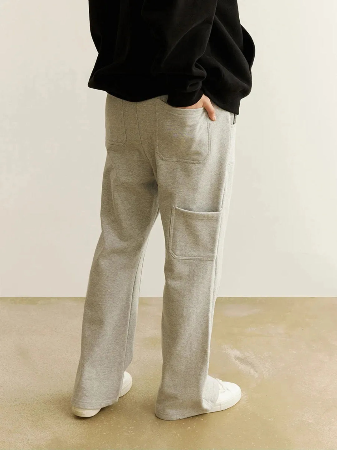 A person wearing gray sweatpants with an elastic waistband and drawcord, featuring patchwork pockets on the thigh.