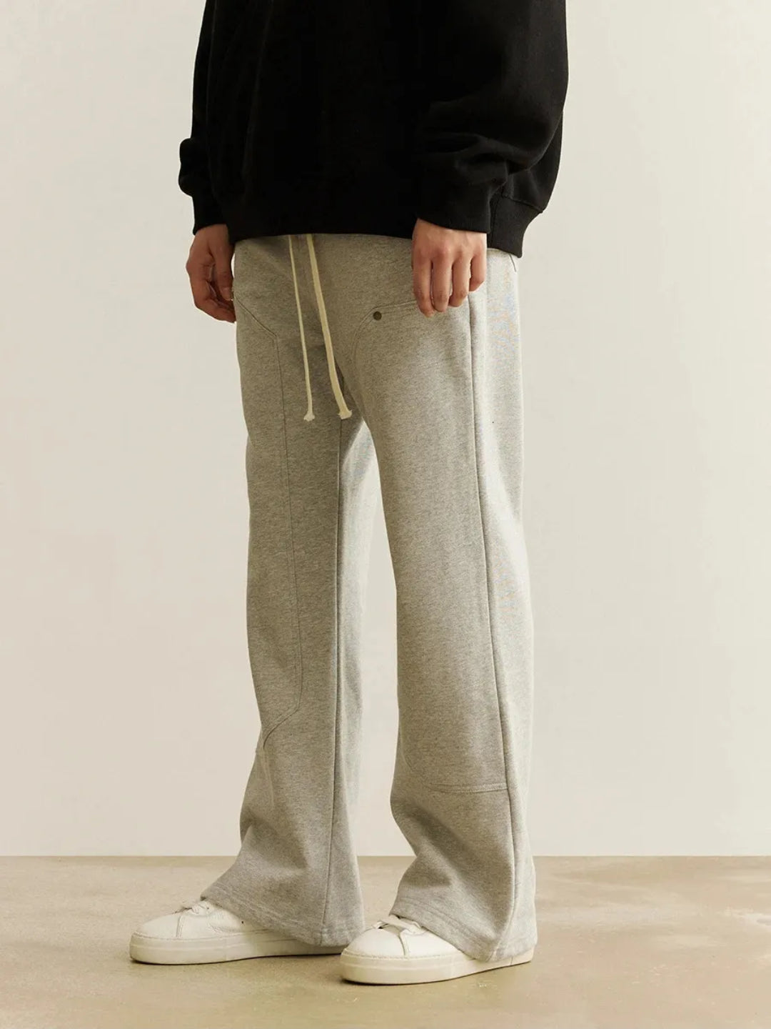 A person wearing gray sweatpants with an elastic waistband and drawcord, featuring patchwork pockets on the thigh.