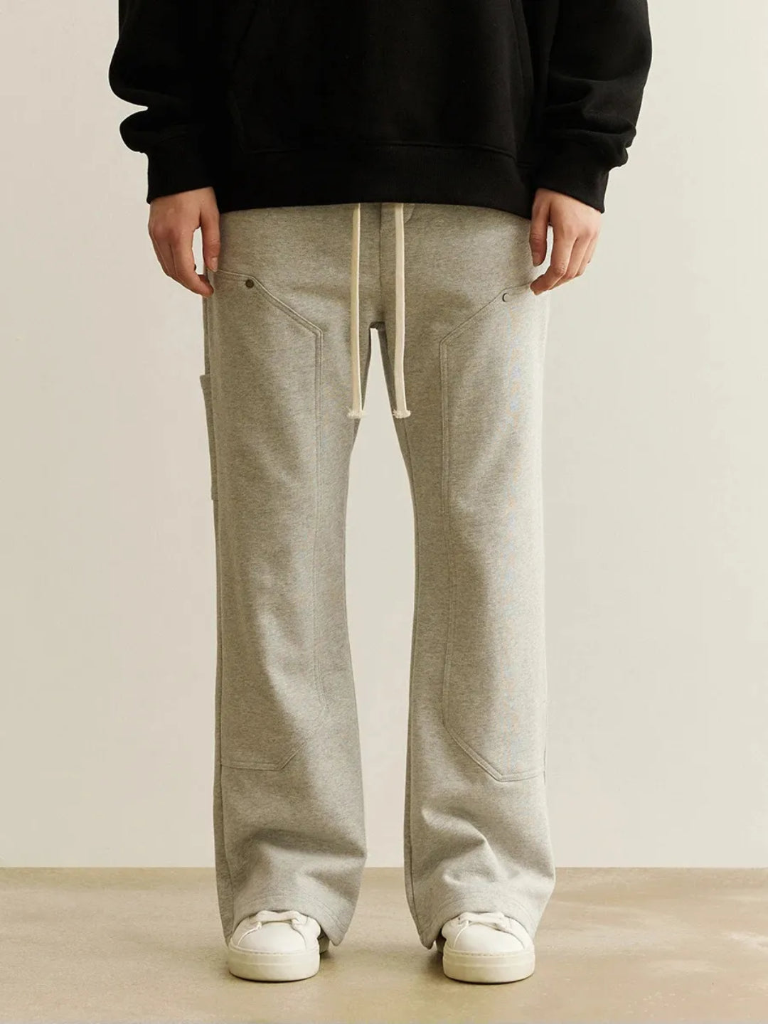 A person wearing gray sweatpants with an elastic waistband and drawcord, featuring patchwork pockets on the thigh.
