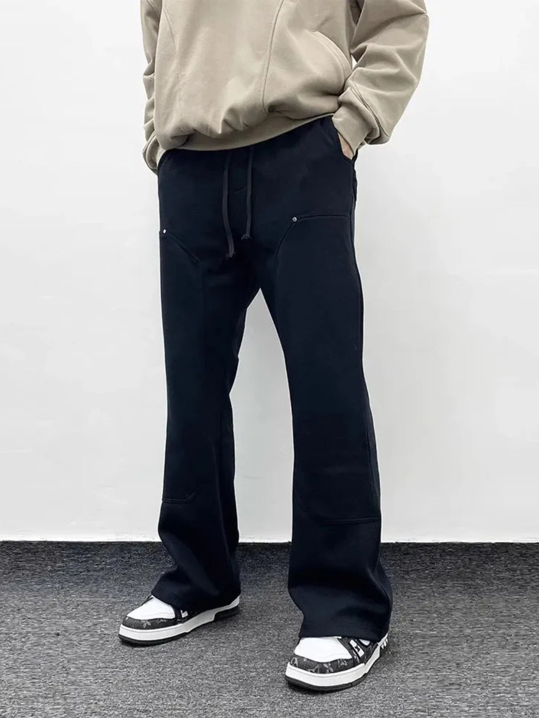 A person wearing blacksweatpants with an elastic waistband and drawcord, featuring patchwork pockets on the thigh.