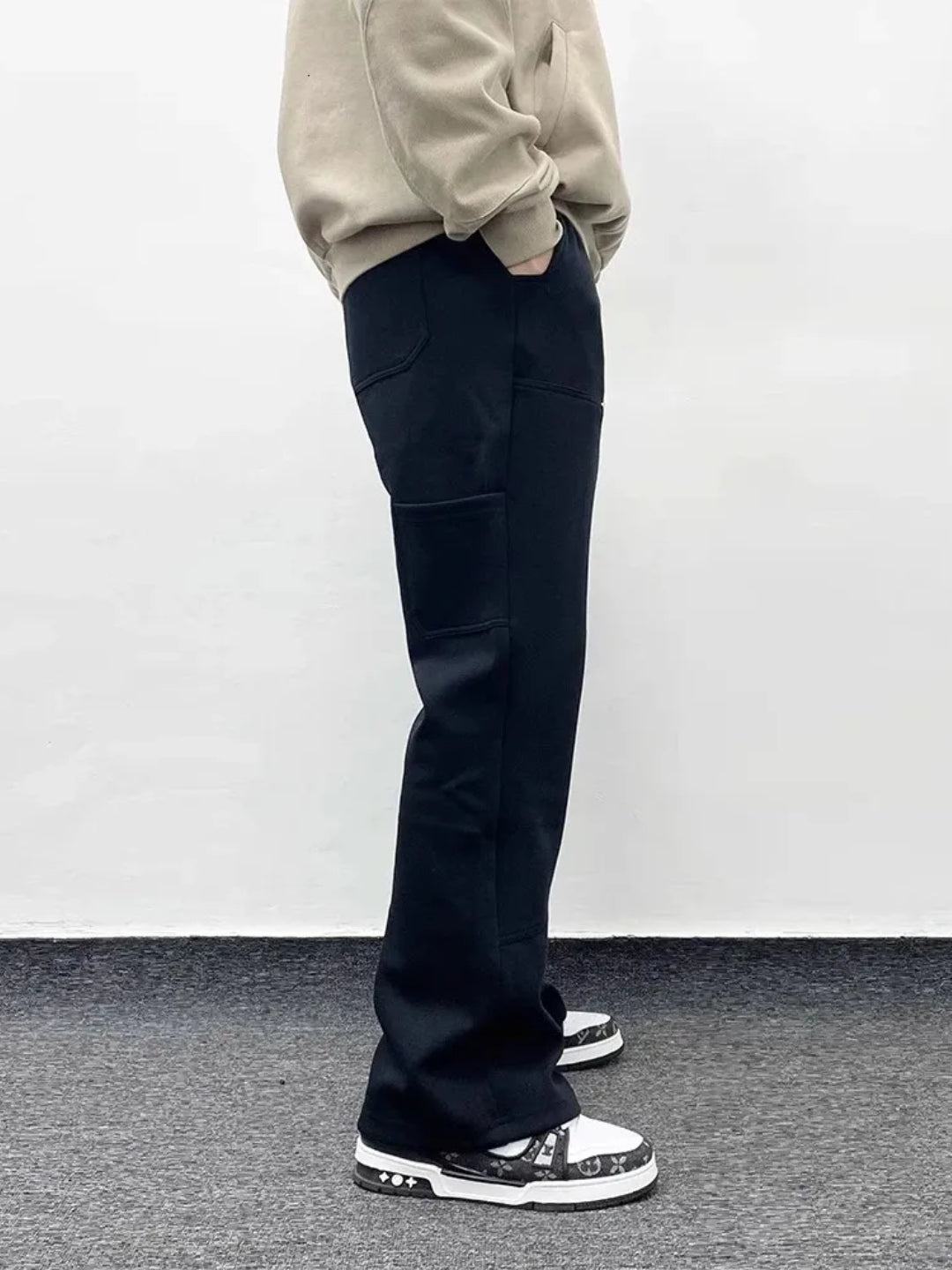 A person wearing blacksweatpants with an elastic waistband and drawcord, featuring patchwork pockets on the thigh.