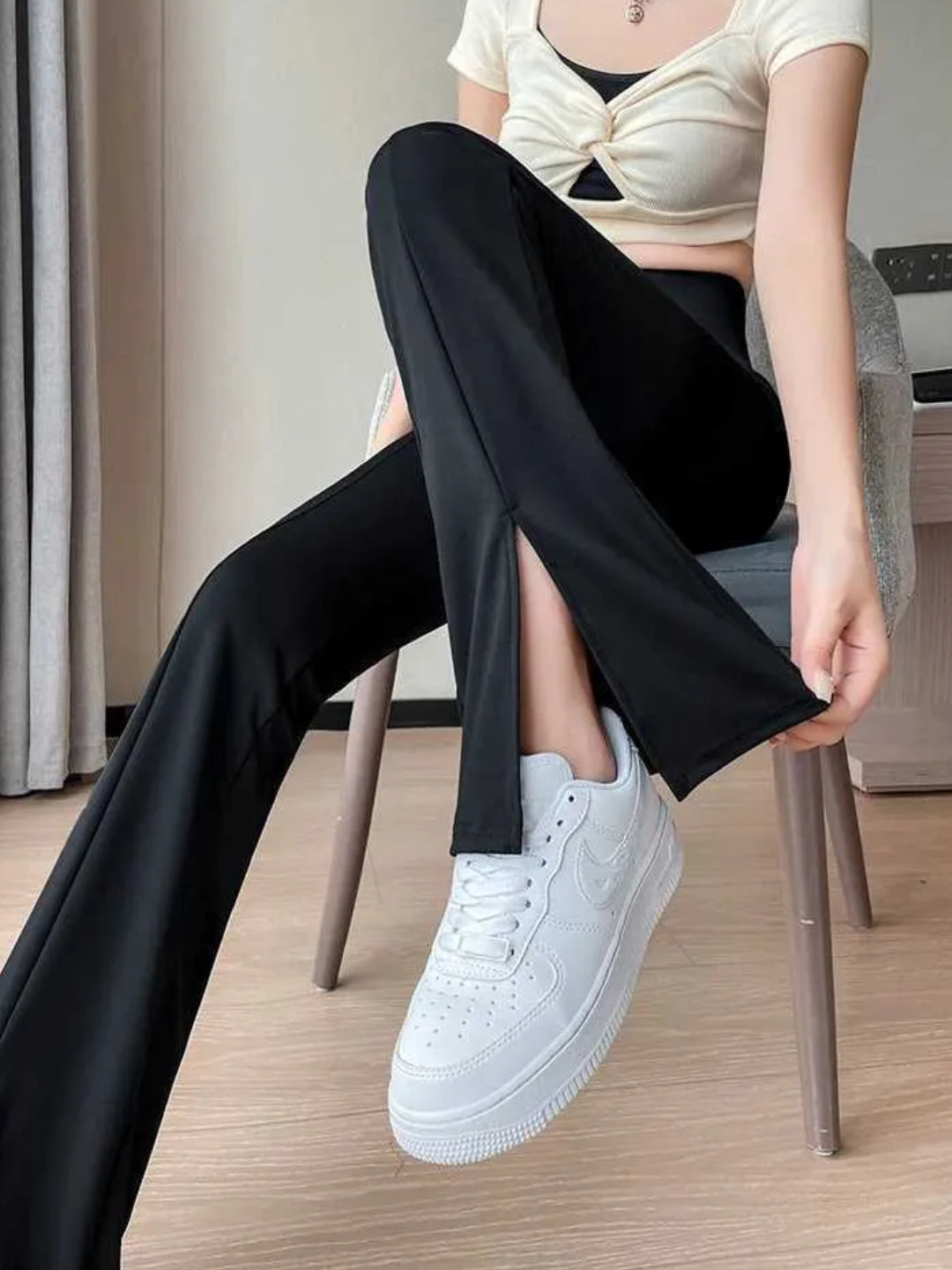 high-waist black yoga pants with a front slit, paired with white sneakers, carrying a white bag, with a decorative lamp in the background.