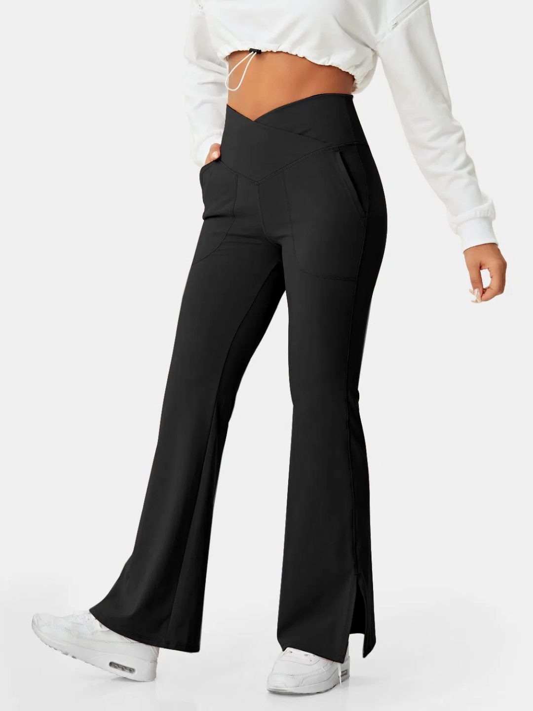 A person wearing black flare leggings with a split hem, paired with a white cropped top and white sneakers.
