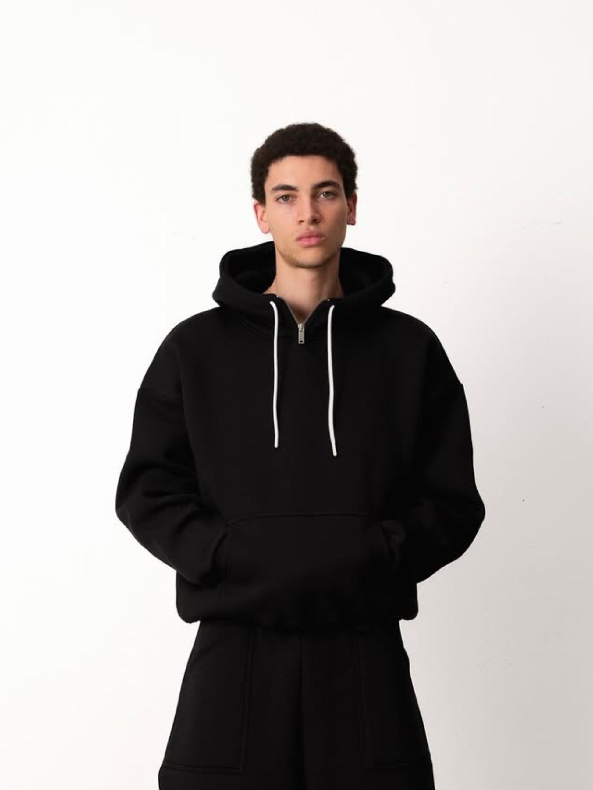 Person wearing a black hoodie with a white zipper on a white background