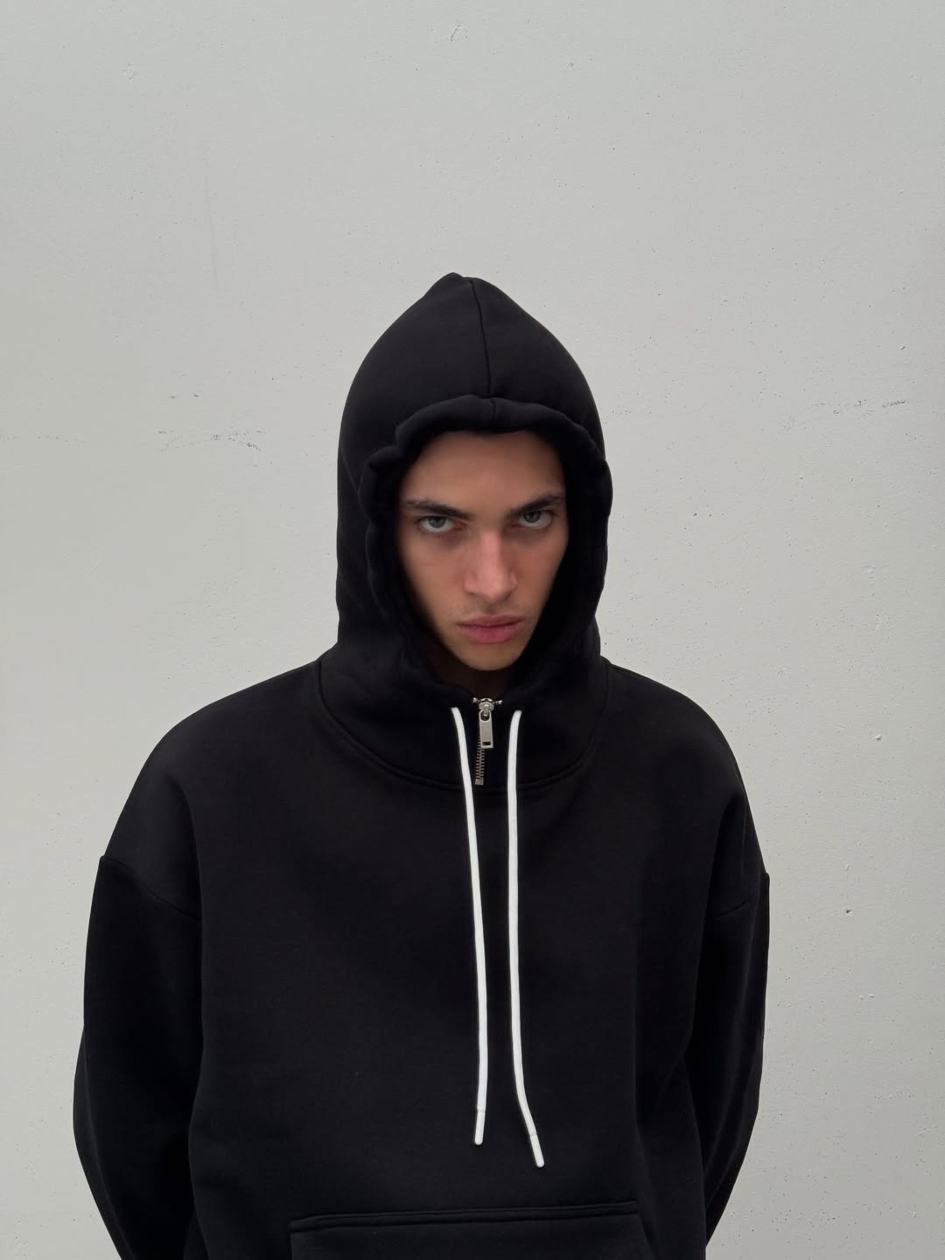 Person wearing a black hoodie with a white zipper on a plain background