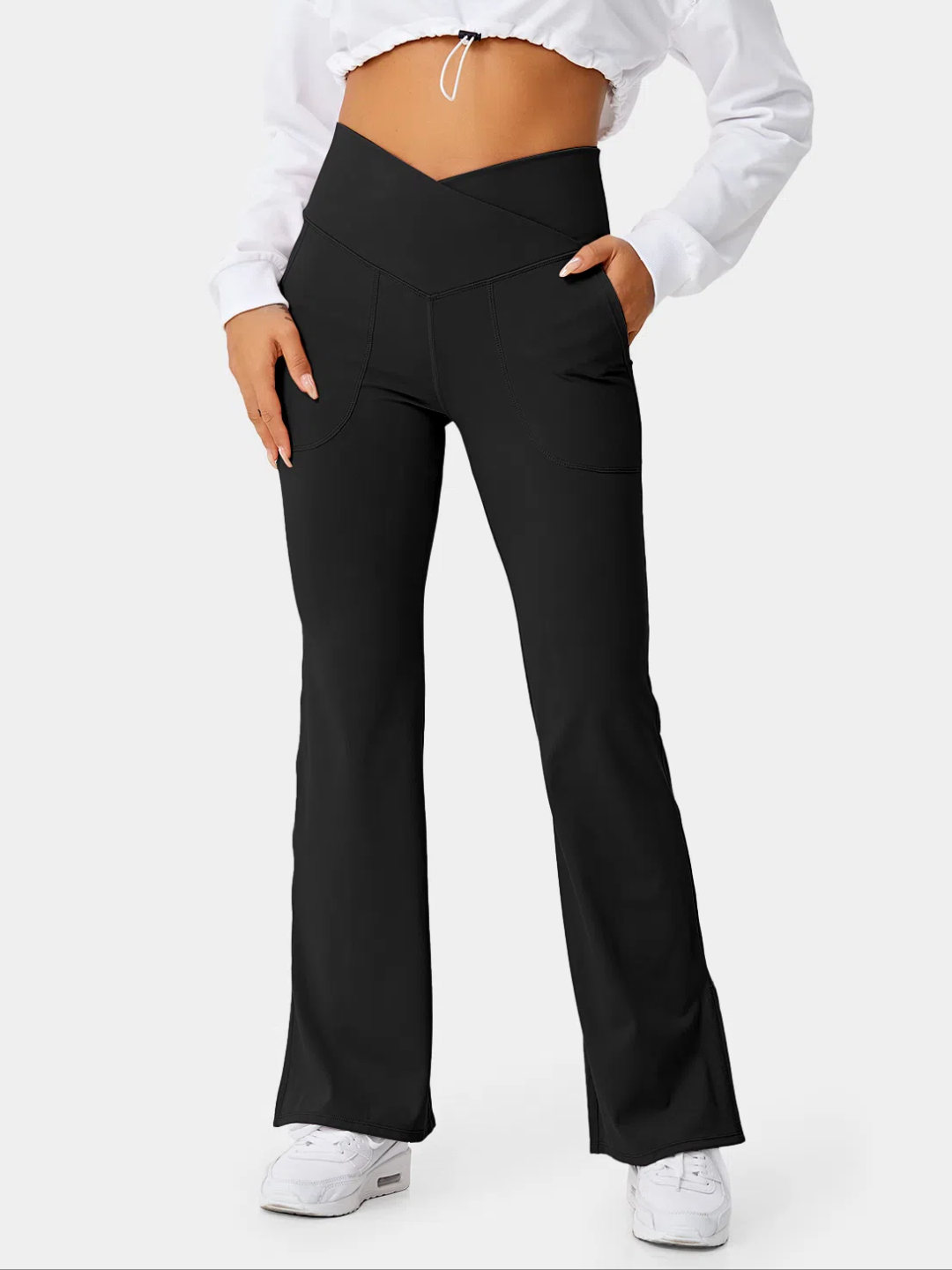 A person wearing black flare leggings with a split hem, paired with a white cropped top and white sneakers.