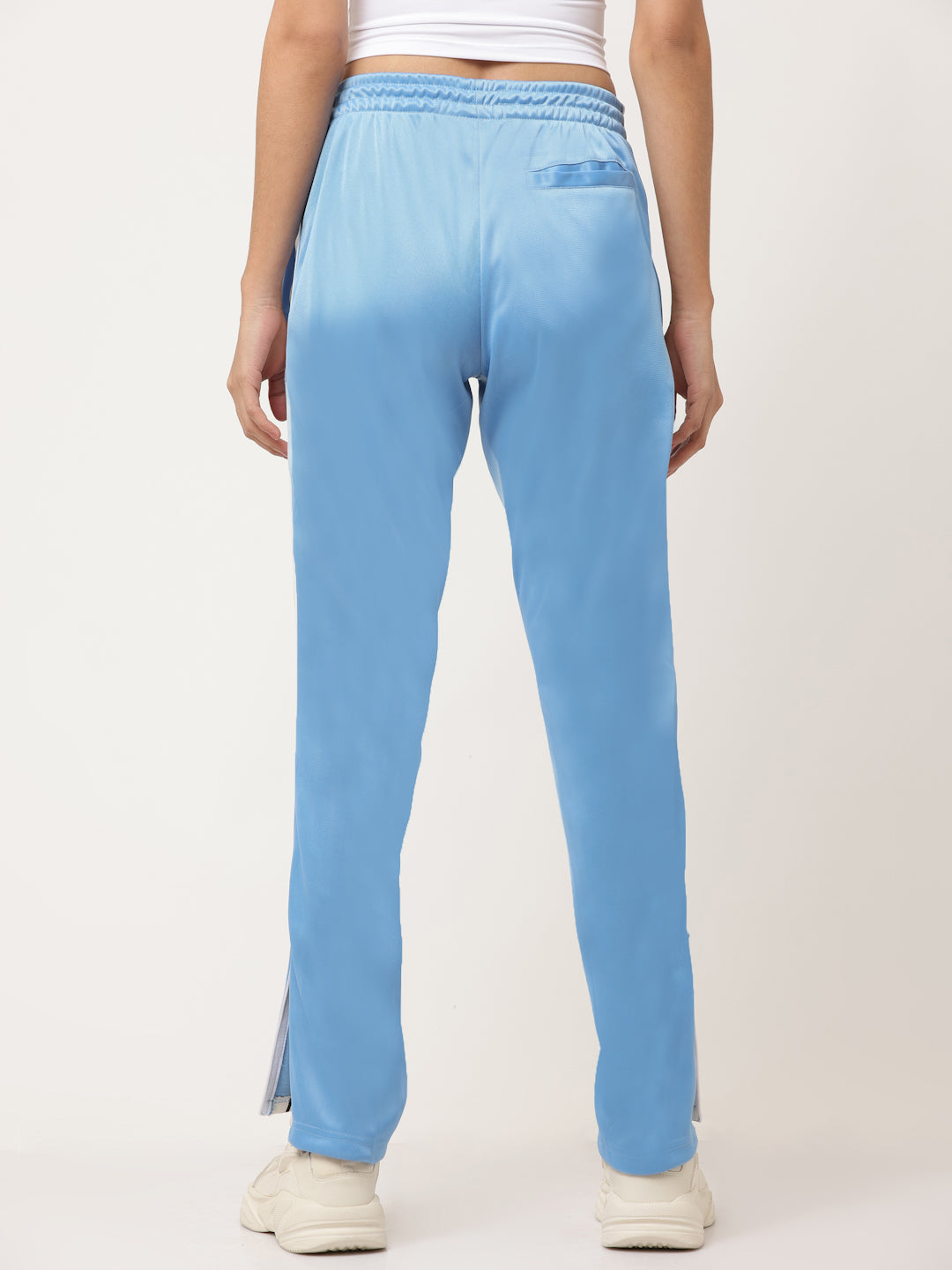 A pair of blue straight fit track pants with white side stripe detailing and a visible zipper at the bottom, held by a model.