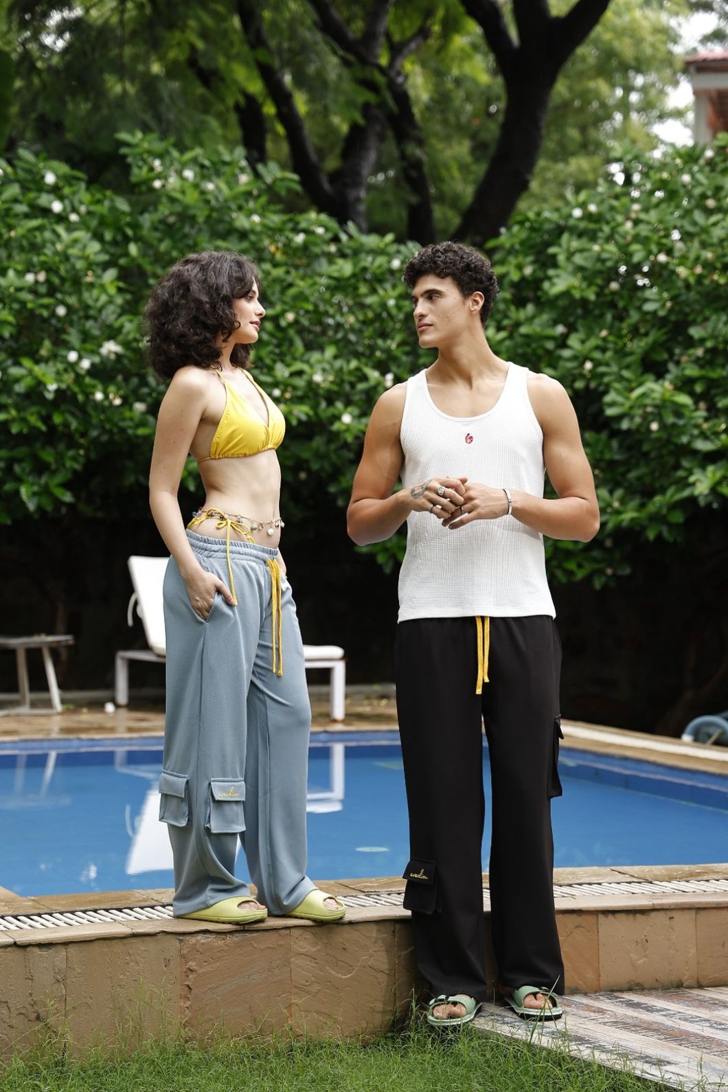 Two people standing by a pool with greenery in the background
