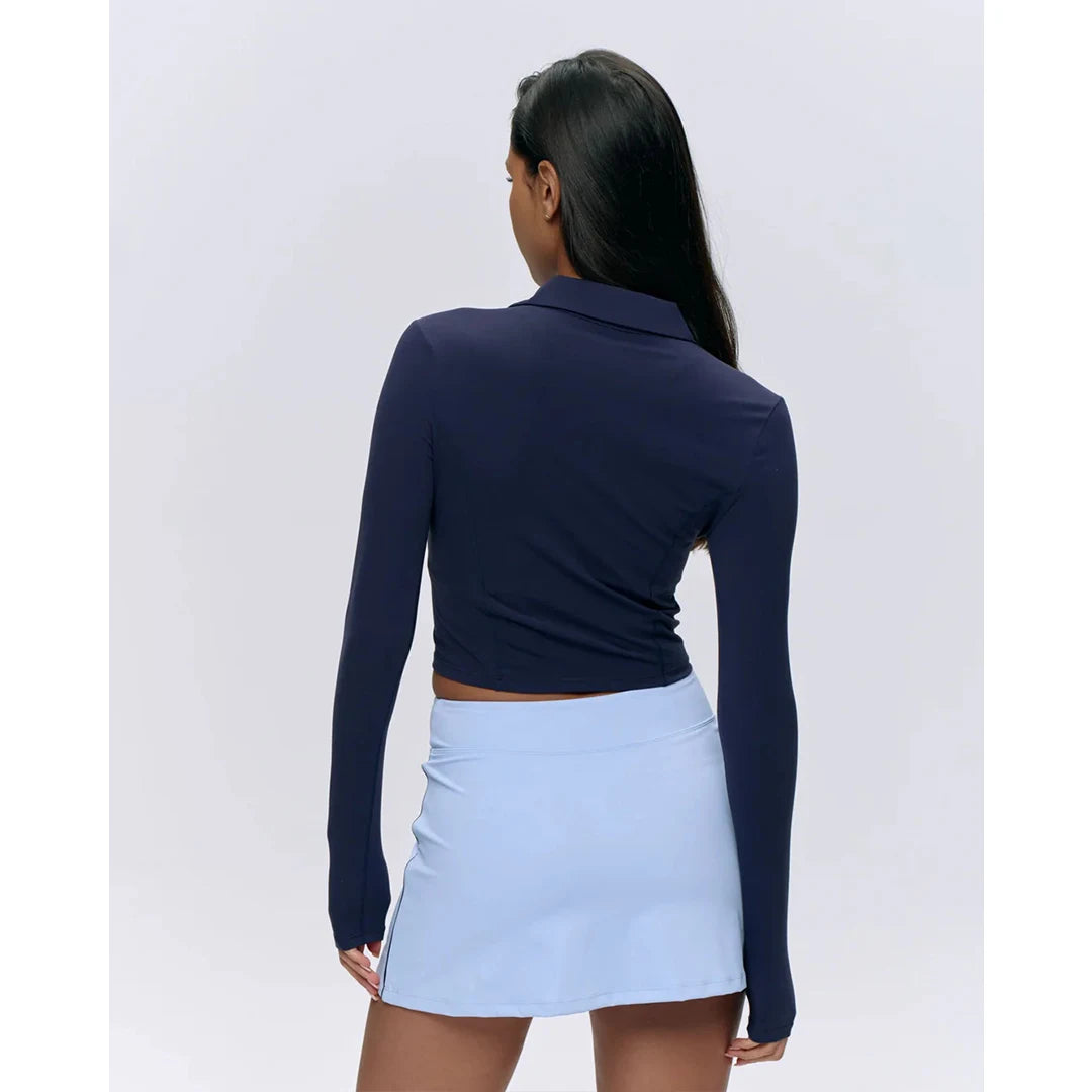 Woman wearing a navy long-sleeve top and light blue skirt on a white background
