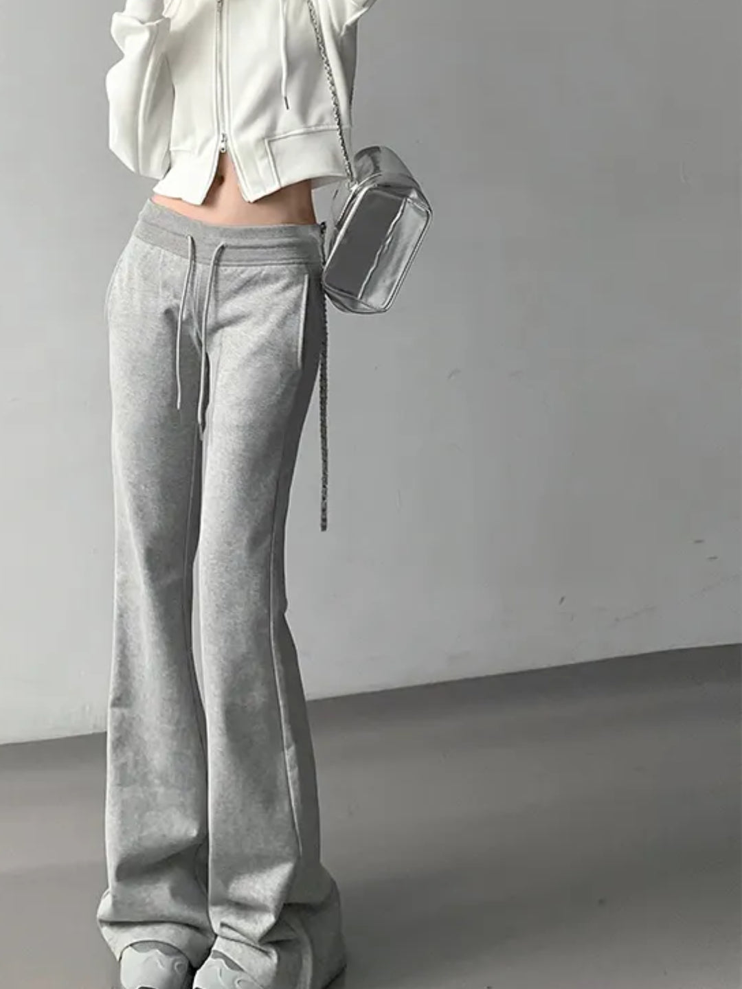A person wearing grey low-rise flared sweatpants and a white hoodie with a visible logo.