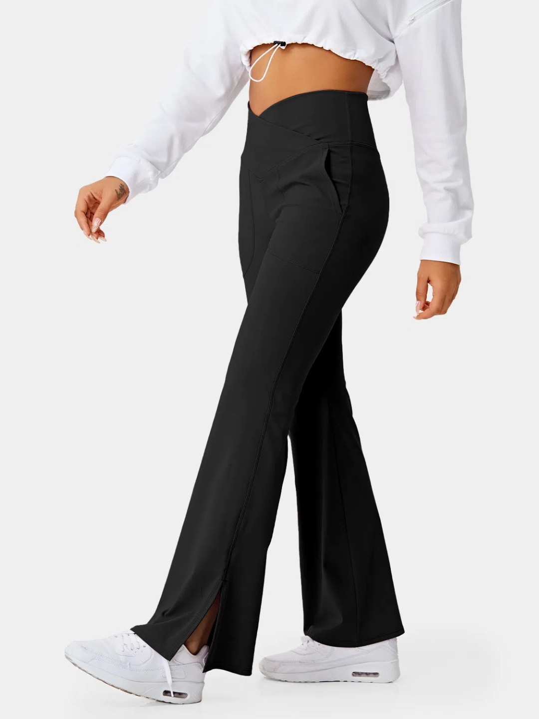 A person wearing black flare leggings with a split hem, paired with a white cropped top and white sneakers.