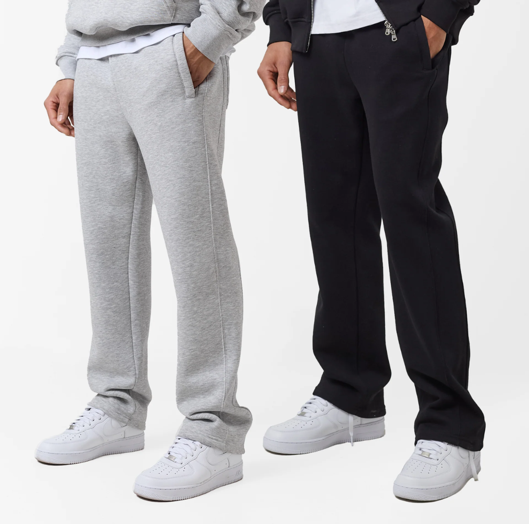 Two pairs of joggers, one in light gray and one in black, with an open hem design, elastic waistbands with drawstrings, and side pockets. Both are paired with white sneakers.