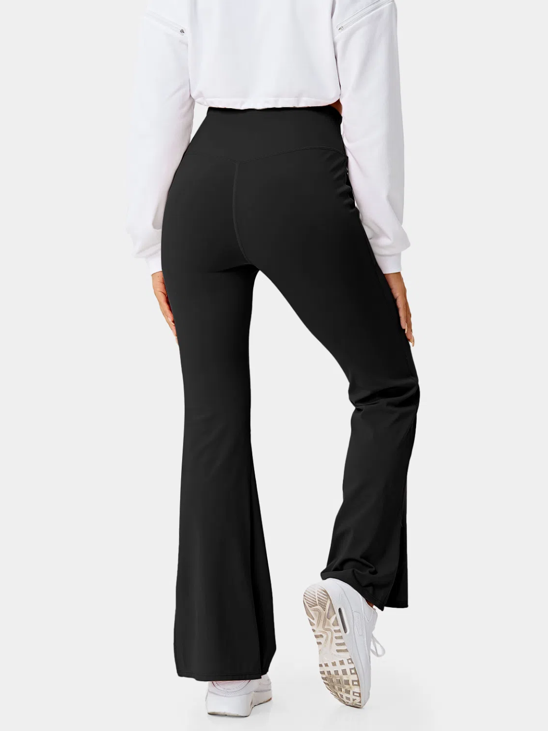 A person wearing black flare leggings with a split hem, paired with a white cropped top and white sneakers.