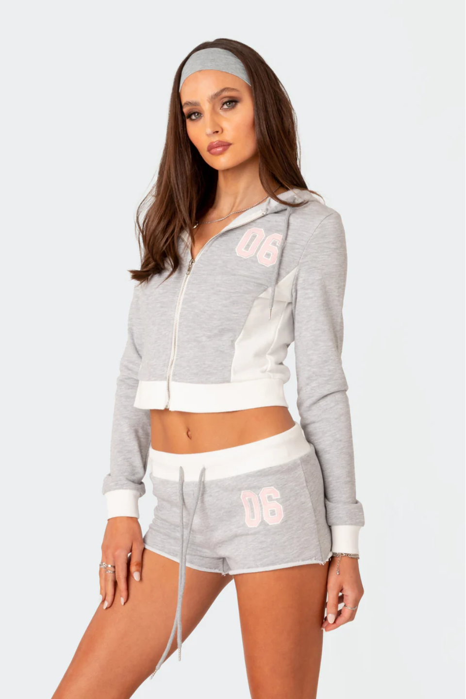 A female model wearing a grey Paparazzi hoodie and matching shorts with a text pattern.