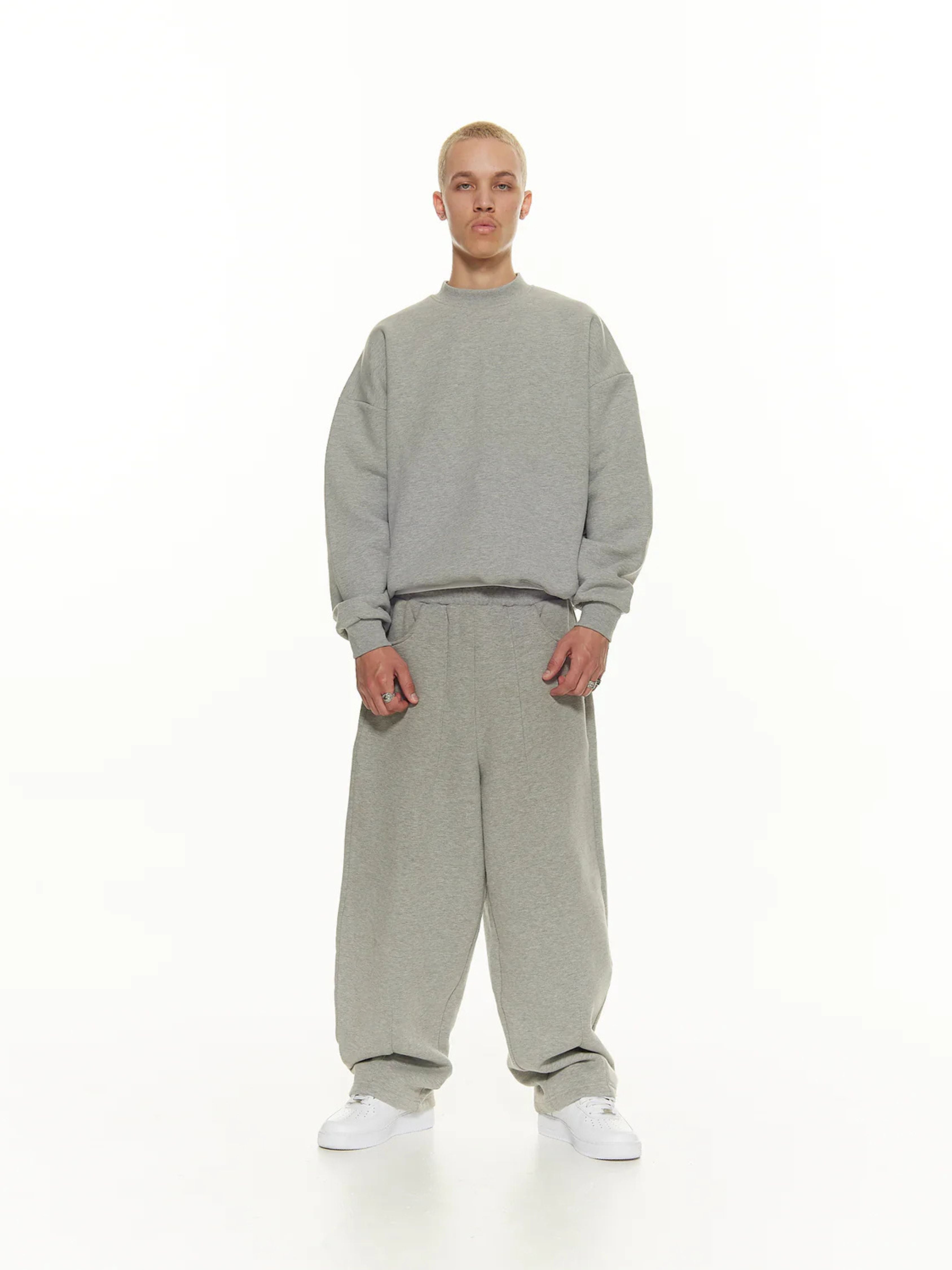 Person wearing a grey sweatshirt and pants set on a white background