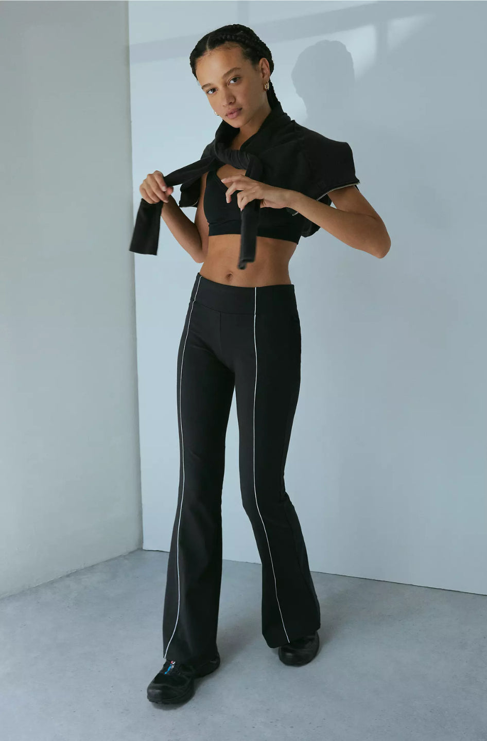 A woman modeling black piped flare pants with a wide fit and high waist.