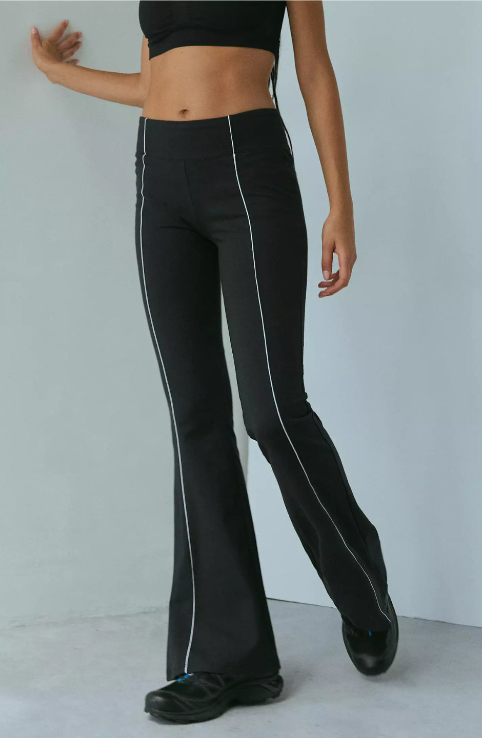 A woman modeling black piped flare pants with a wide fit and high waist.