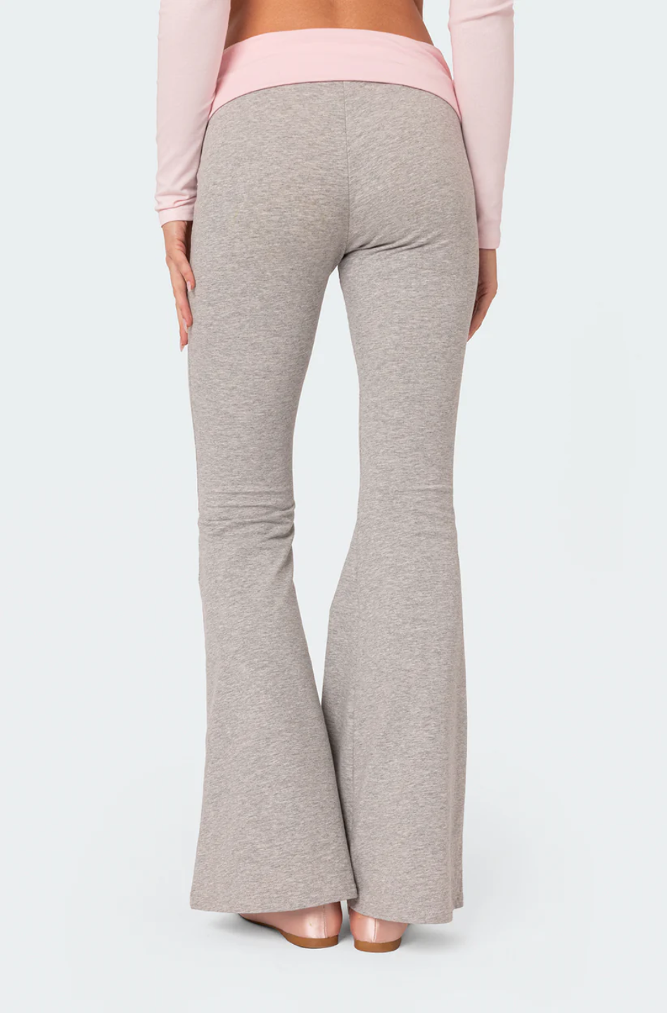 A female model wearing a pink rhinestone top with long sleeves, paired with gray flare leggings. She is also holding a small white purse.