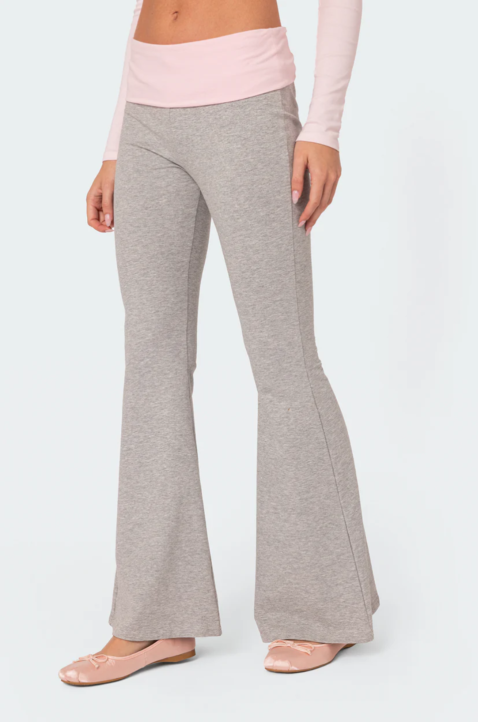 A female model wearing a pink rhinestone top with long sleeves, paired with gray flare leggings. She is also holding a small white purse.